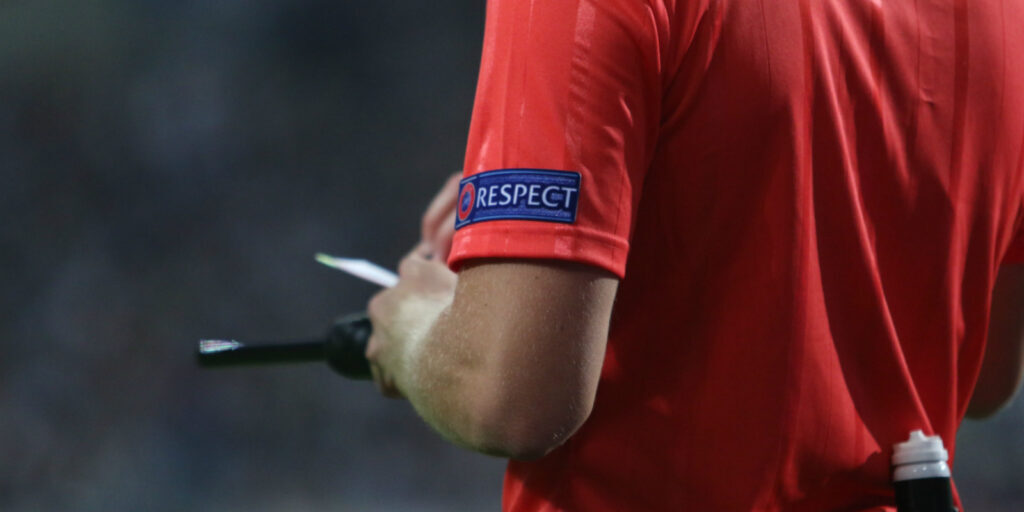 Braço de um árbitro de equipamento vermelho com o símbolo Respect da UEFA, a escrever num cartão